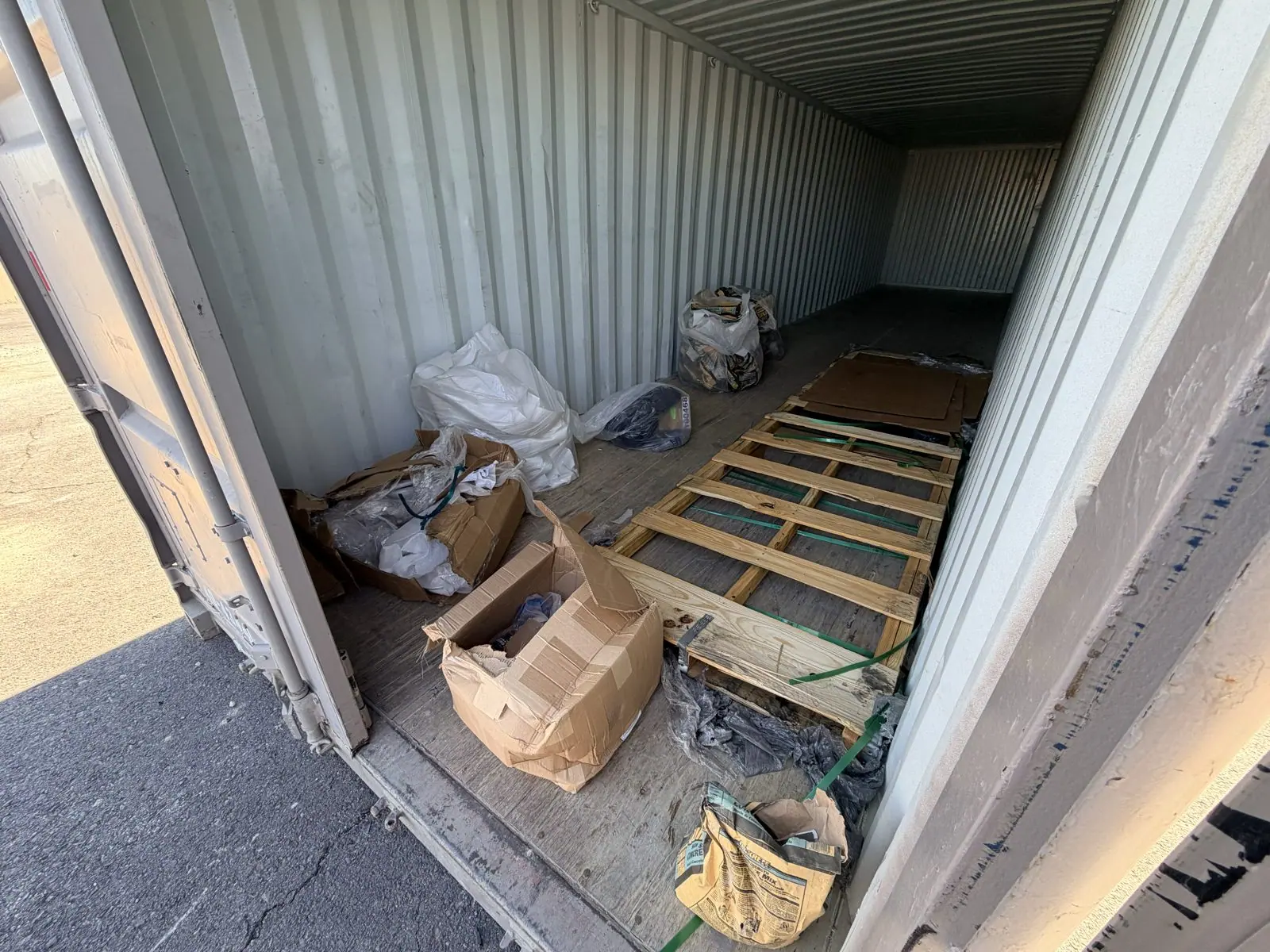 Shipping container holding broken pallets, cardboard boxes and bagged trash before a commercial cleanout