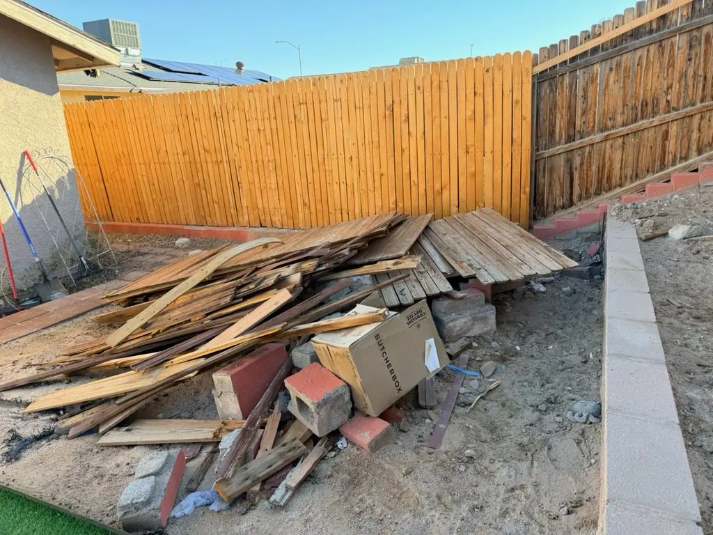Henderson backyard corner piled with old fence boards, broken pickets and concrete-filled bricks left by a fence contractor